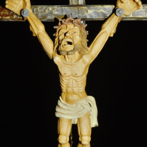 Ein Kruzifixus zeigt einen leidenden Christus am Kreuz vor schwarzem Hintergrund.