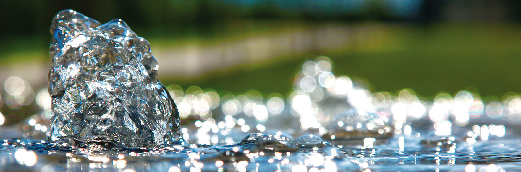 Ein klarer Wassertropfen erzeugt beim Aufprall kreisförmige Wellen und glitzernde Lichtreflexe im.