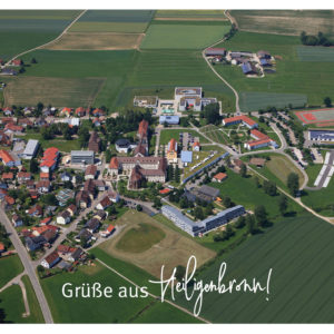 Heiligenbronn zeigt eine ländliche Gemeinde mit Kirche, Schule und Feldern unter leicht bewölktem.