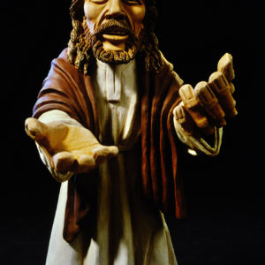 Jesusfigur aus Ton mit ernstem Blick und ausgestreckten Händen vor schwarzem Hintergrund.