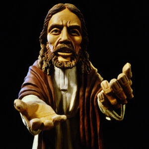 Jesusfigur aus Ton mit ernstem Blick und ausgestreckten Händen vor schwarzem Hintergrund.
