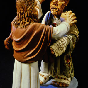Eine Skulptur zeigt Jesus, der einem Kranken die Stirn berührt, vor schwarzem Hintergrund.