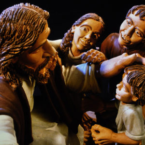 Eine Tonskulptur zeigt Jesus mit Kindern und einer Frau in dramatischer Beleuchtung.
