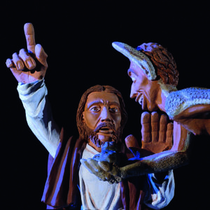 Eine Tonskulptur zeigt einen Mann und eine dämonische Figur in dramatischer Beleuchtung.