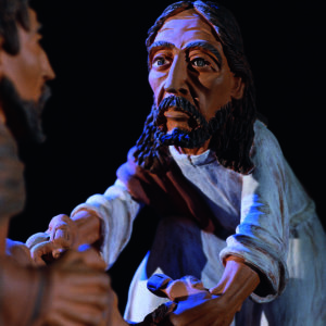 Eine handgefertigte Tonfigur zeigt Jesus Christus mit erhobener Hand vor dunklem Hintergrund.