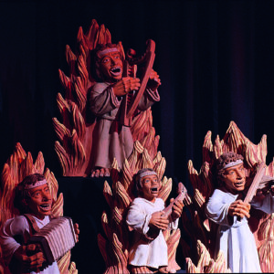 Musizierende Figuren in warmen Farben sind theatralisch vor dunklem Hintergrund dargestellt.