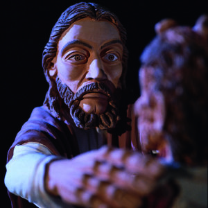 Eine dunkle Tonskulptur zeigt Jesus Christus mit ausgestreckter Hand vor schwarzem Hintergrund.