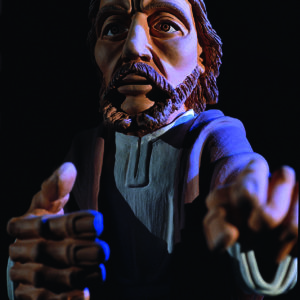 Eine beleuchtete Jesusfigur aus Ton tritt aus der Dunkelheit hervor und blickt zum Betrachter.