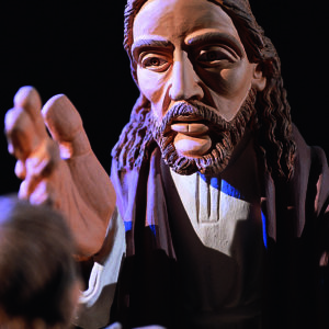 Eine Jesusfigur mit ausgestreckter Hand wird dramatisch vor schwarzem Hintergrund.