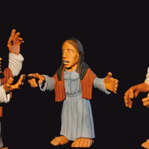 Drei Tonfiguren – Mann, Frau, verschleierte Frau – stehen vor schwarzem Hintergrund auf Sockeln.
