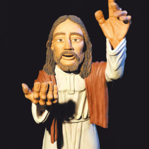Eine detailreiche Jesus-Statue mit erhobener Hand vor schwarzem Hintergrund.