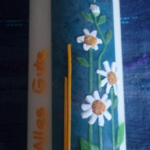 Eine handgefertigte Kerze mit Blumenmuster und goldenem Schriftzug "Alles Gute" dient als.