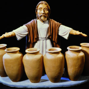 Die Skulptur zeigt Jesus bei der Hochzeit zu Kana vor Tonkrügen, betont durch Licht.