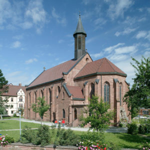 Das Kloster Heigenbronn zeigt eine rote Kirche mit Turm, umgeben von Natur und Gebäuden.