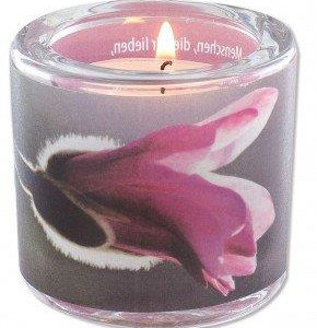 Eine cremefarbene Kerze in Glas zeigt eine große, pinkfarbene Orchideenblüte und rosafarbene.