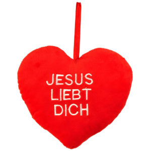 Ein rotes Plüschherz mit der Aufschrift "JESUS LIEBT DICH" hängt vor weißem Hintergrund.