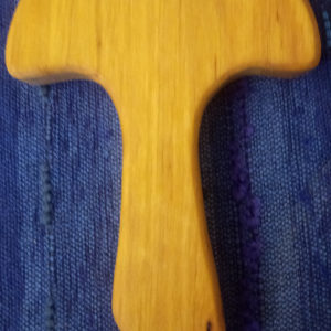 Ein hellbrauner, geschnitzter Holzbuchstabe „T“ liegt auf blauem Stoff, bereit zum Aufhängen.