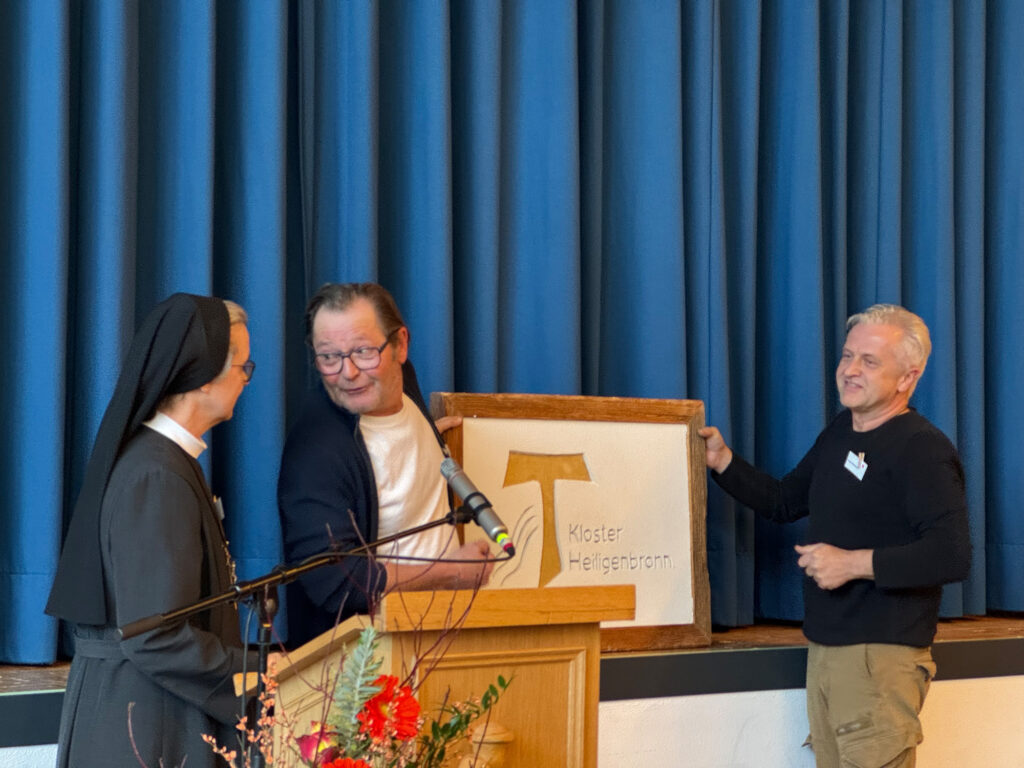 Herr Wenzler (links) und Herr Widmann überreichen Sr. Dorothea eine Tafel mit dem Logo des Klosters